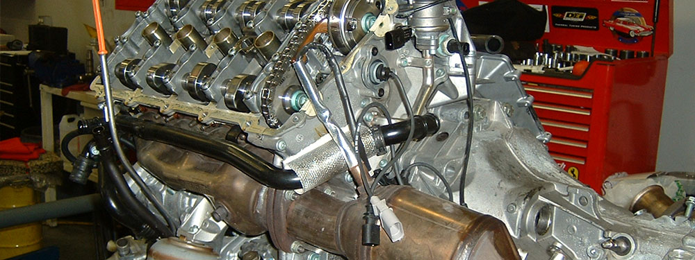 A partly dismantled V-engine on a workshop bench with its camshafts and timing chain exposed, a tool chest behind it.