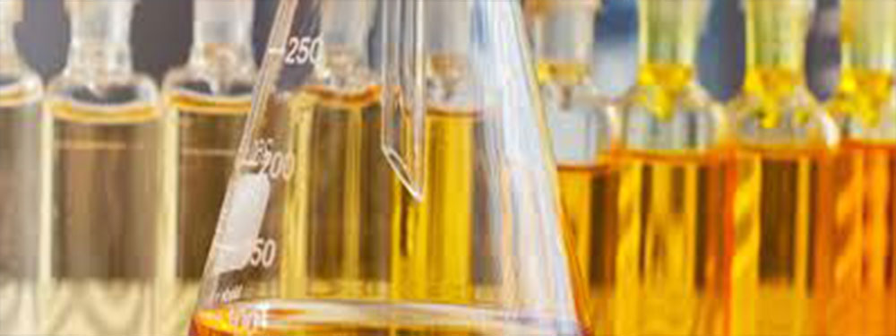 A laboratory flask of amber fluid in front of rows of graduated sample vials.