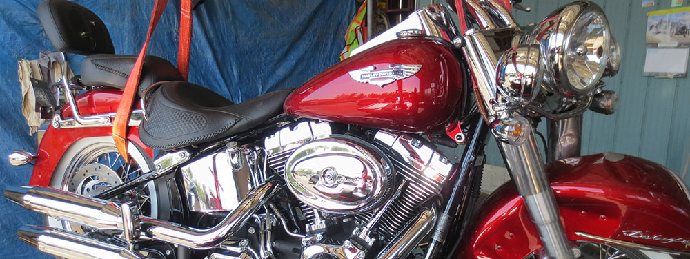 A red motorcycle held upright by ratchet straps in front of a tarpaulin.